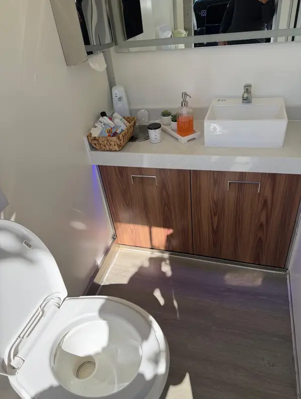 Restroom trailer interior with a flush toilet, wood vanity and vessel sink