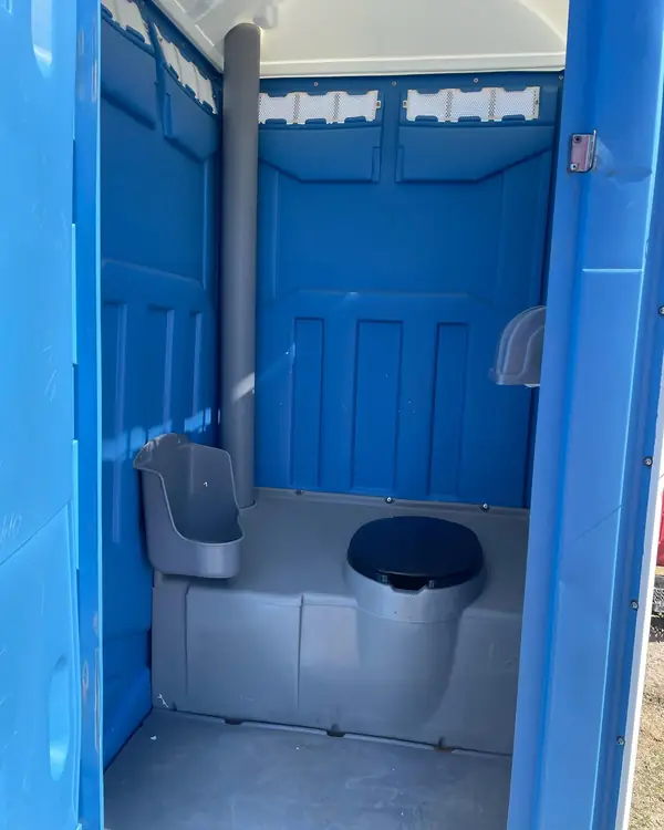 Inside a standard porta potty showing the toilet seat, urinal and vent pipe